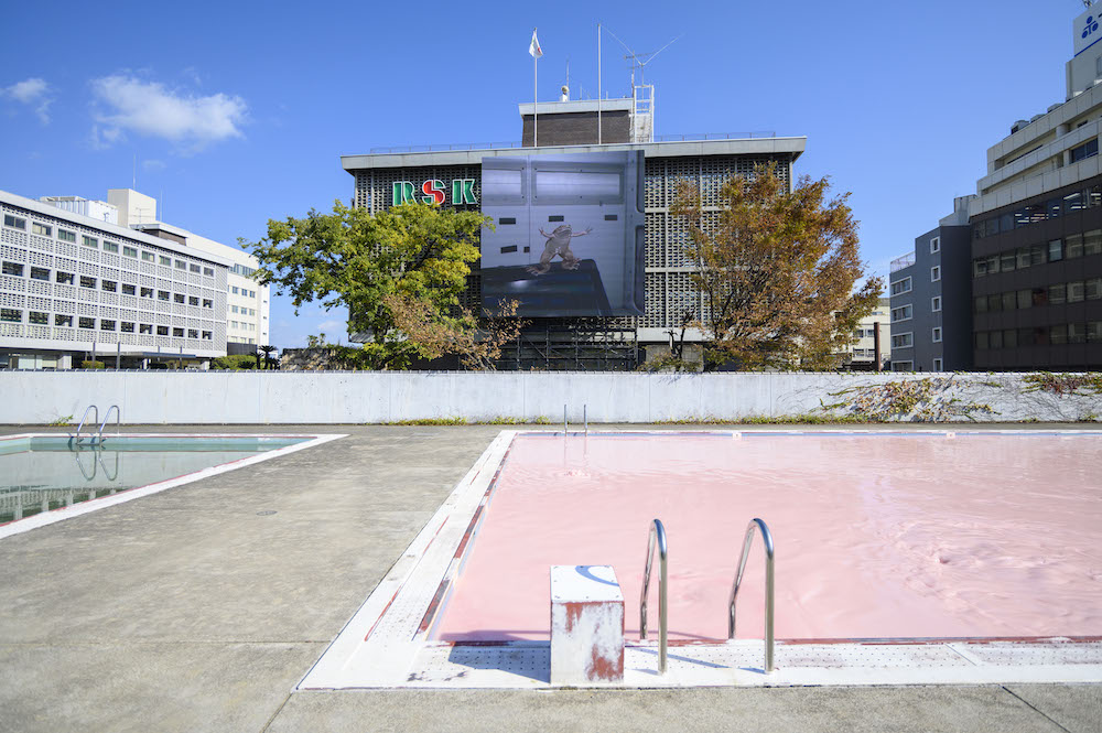 会場のひとつ、旧内山下小学校のプールや、向かいの山陽放送の巨大サイネージも作品に変貌しました (2019年撮影)